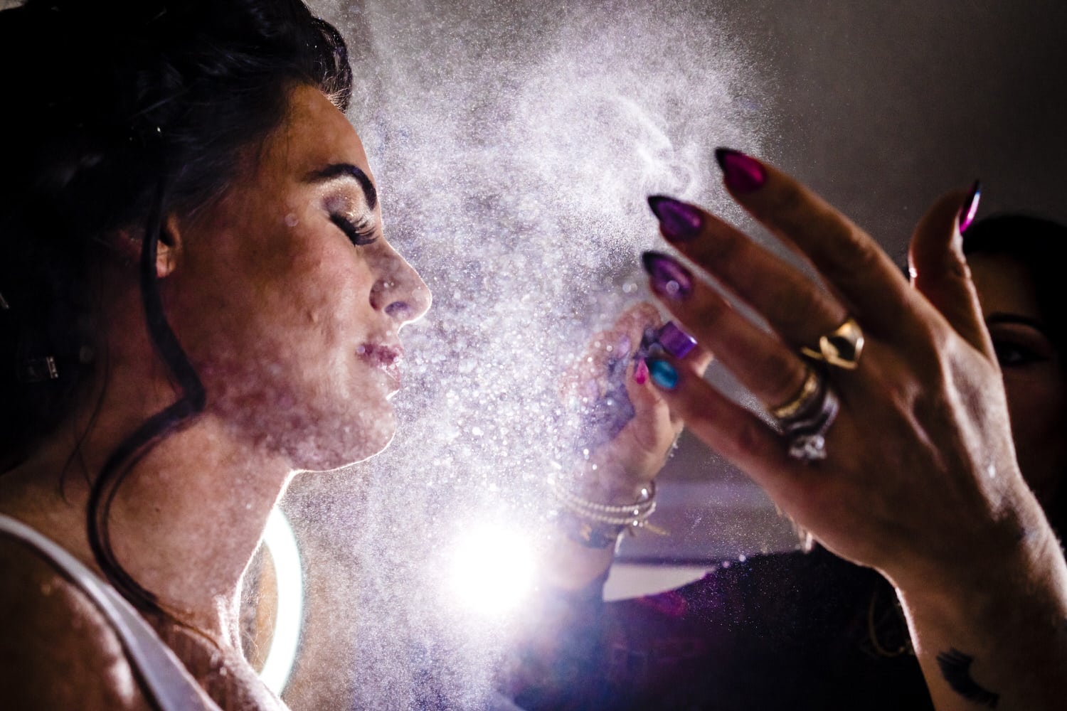 A colorful, closeup picture of a makeup artist spraying finishing spray on a bride's face. 