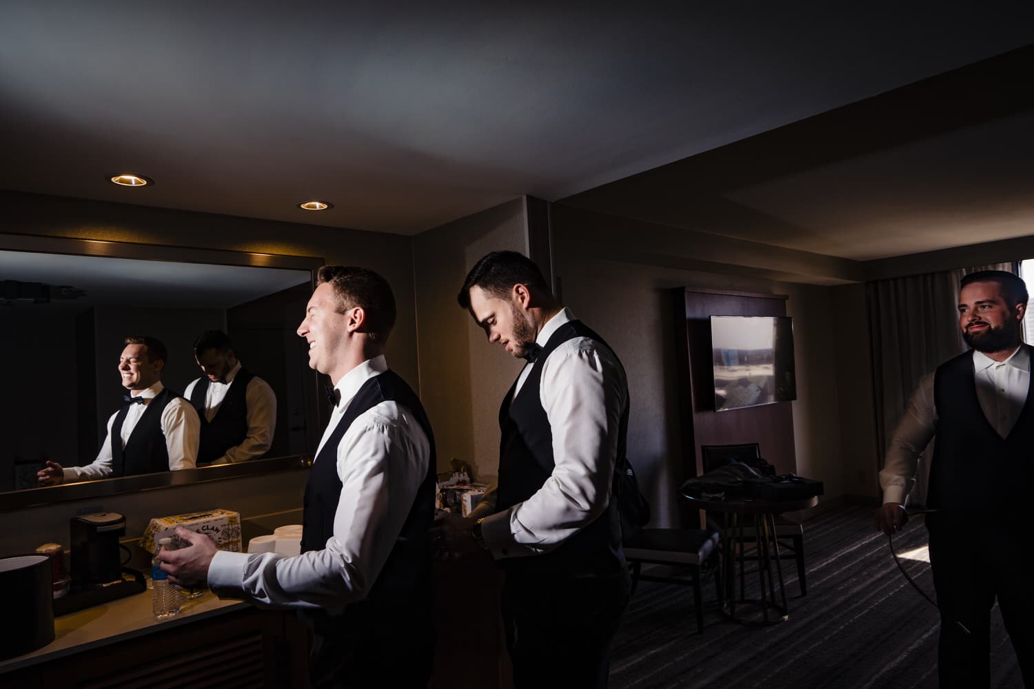 A picture of two groomsmen laughing helping each other get dressed on the morning of a winter wedding in Kansas City. 