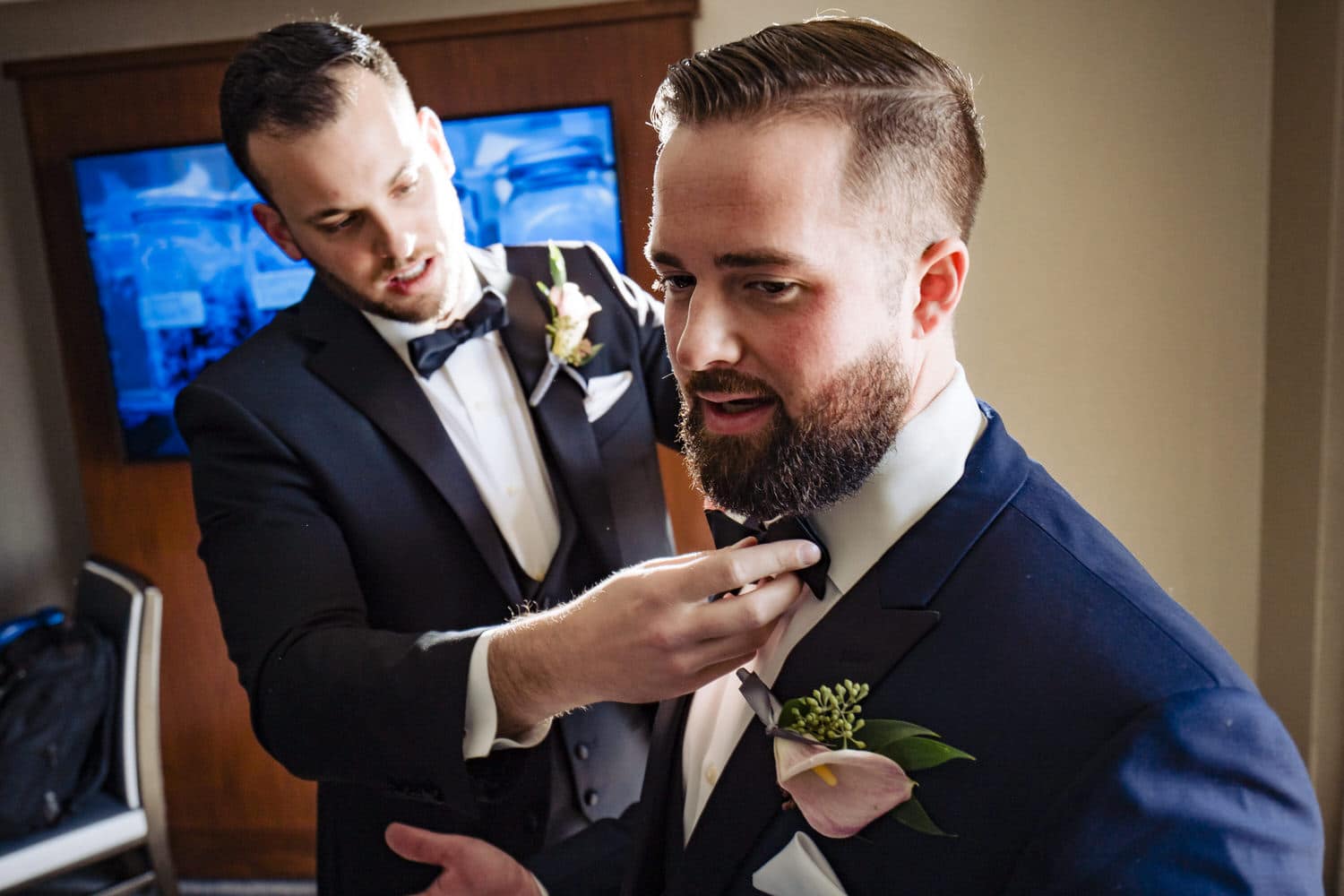 A candid picture of a groomsman adjusting a groom's bow tie on the morning of his winter wedding. 