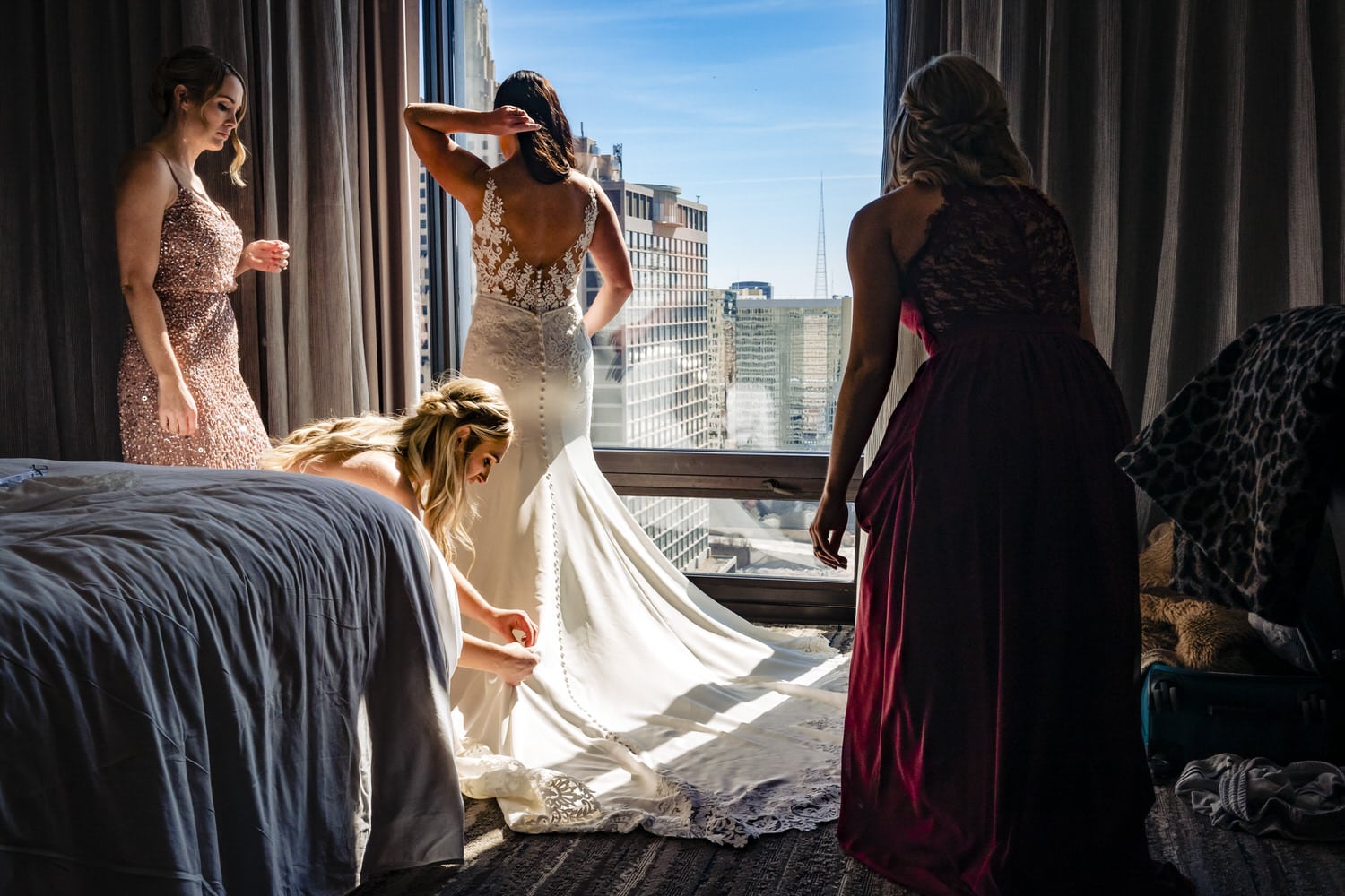 A colorful, candid picture of three bridesmaids adjusting their sister's wedding gown. 