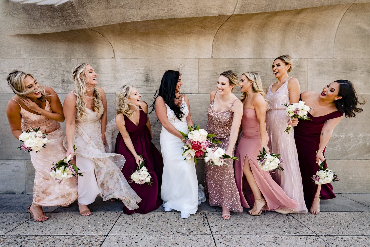 A colorful, candid picture of a bride and her bridesmaids looking at each other and laughing on a windy winter wedding day in Kansas City. 