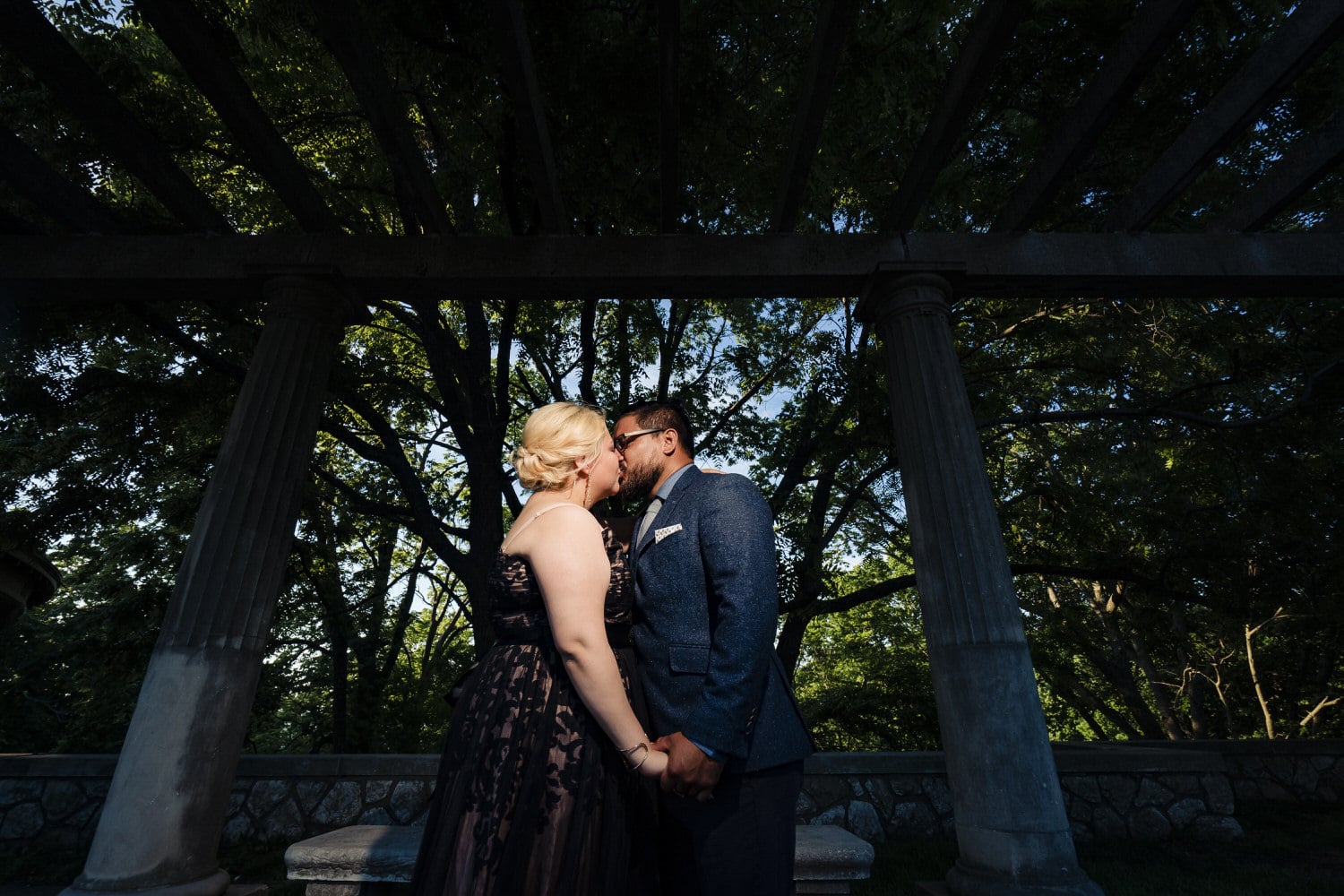 A vibrant portrait of a man and woman kissing against a canopy of trees during their romantic engagement session in Kansas City. 