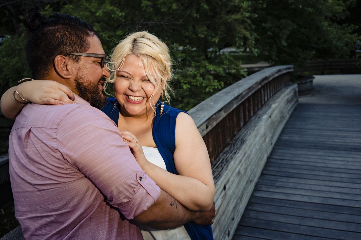 A colorful picture of an engaged couple sharing an embrace while standing on a wooden bridge during their Loose Park engagement session in Kansas City. 