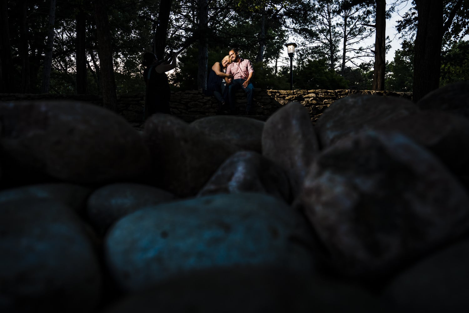 A wide picture of a man and woman sitting on a stone ledge  during a Loose Park engagement session in Kansas City. 
