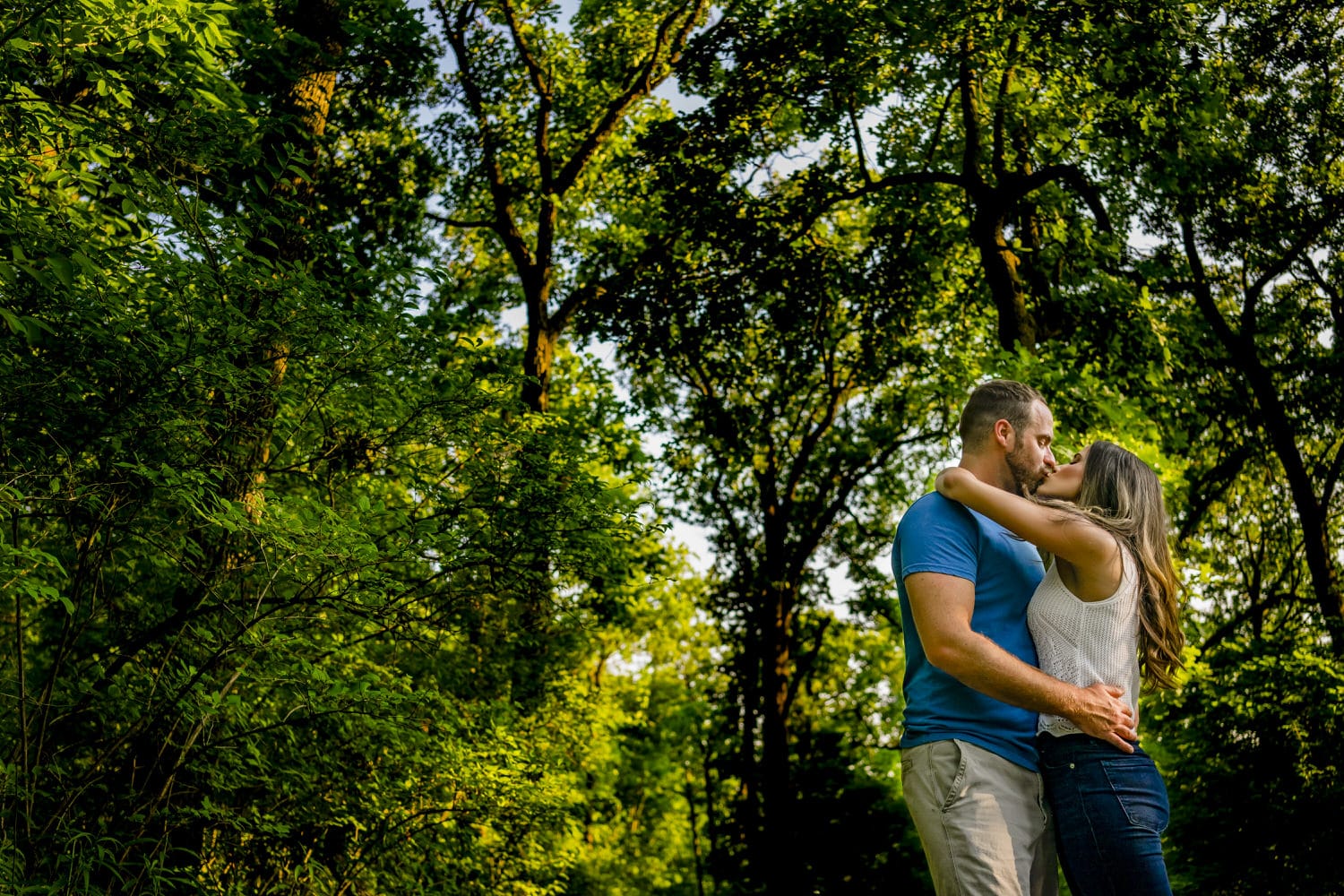A colorful, candid picture of an engaged couple sharing a kiss and embrace during their summer engagement session in Kansas City. 