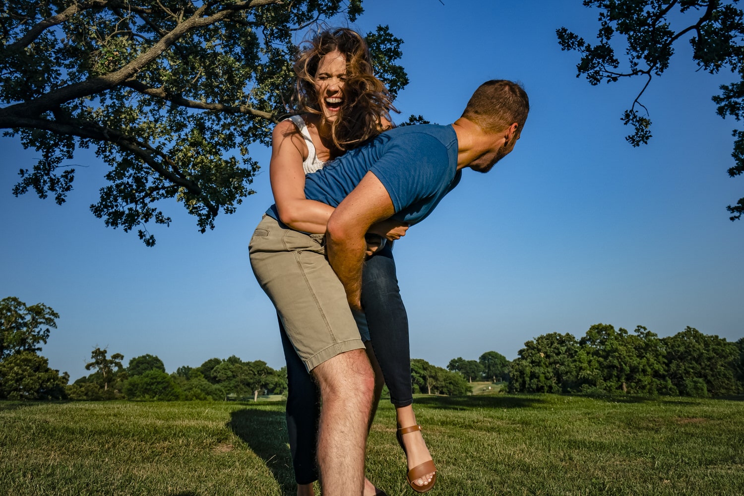 A colorful, candid picture of an engaged couple sharing an embrace and laughing together during their summer engagement session in Kansas City at Swope Park. 