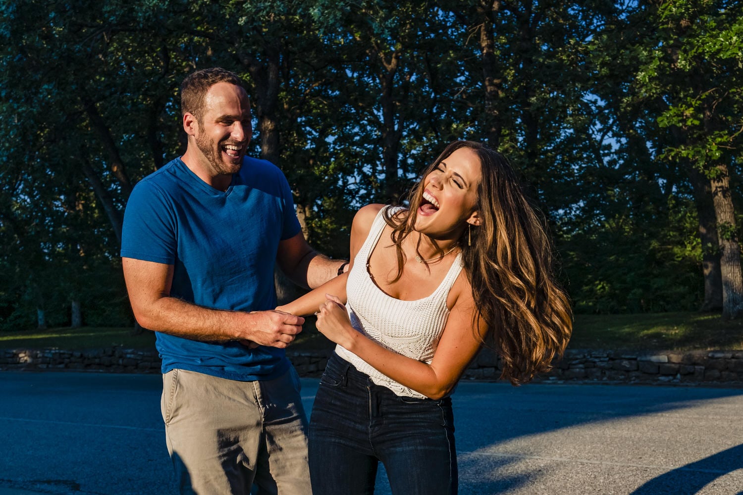 A colorful, candid picture of an engaged couple sharing an embrace and laughing together during their summer engagement session in Kansas City at Swope Park. 