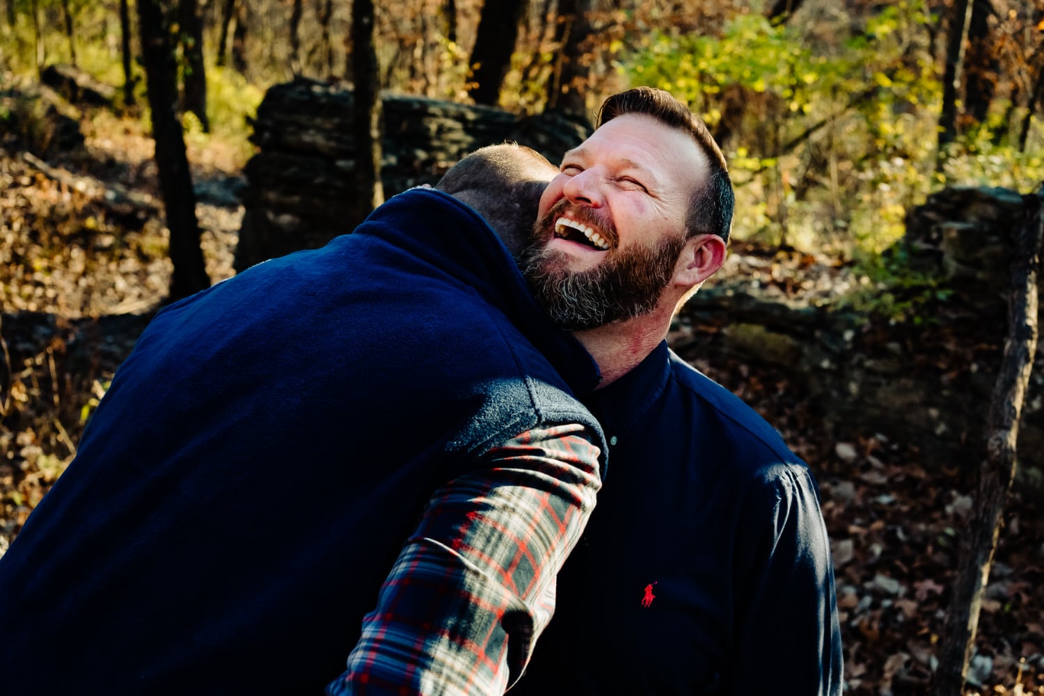 A candid picture of an engaged couple in flannel shirts leaning in to share an embrace during their woodsy engagement session in Kansas City. 