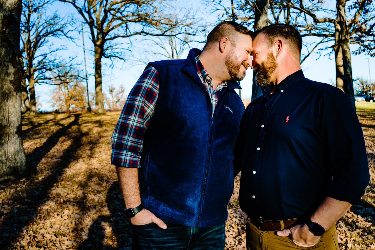 A colorful, candid picture of an engaged couple in navy blue and flannel leaning their heads together smiling at each other during a fall engagement session in Kansas City at Swope Park. 