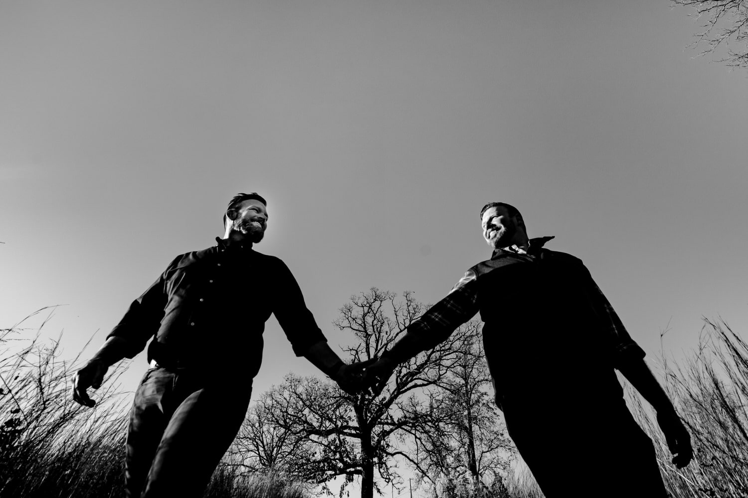 A candid black and white picture of an engaged couple holding hands and smiling at each other as they walk through a field during a fall engagement session. 