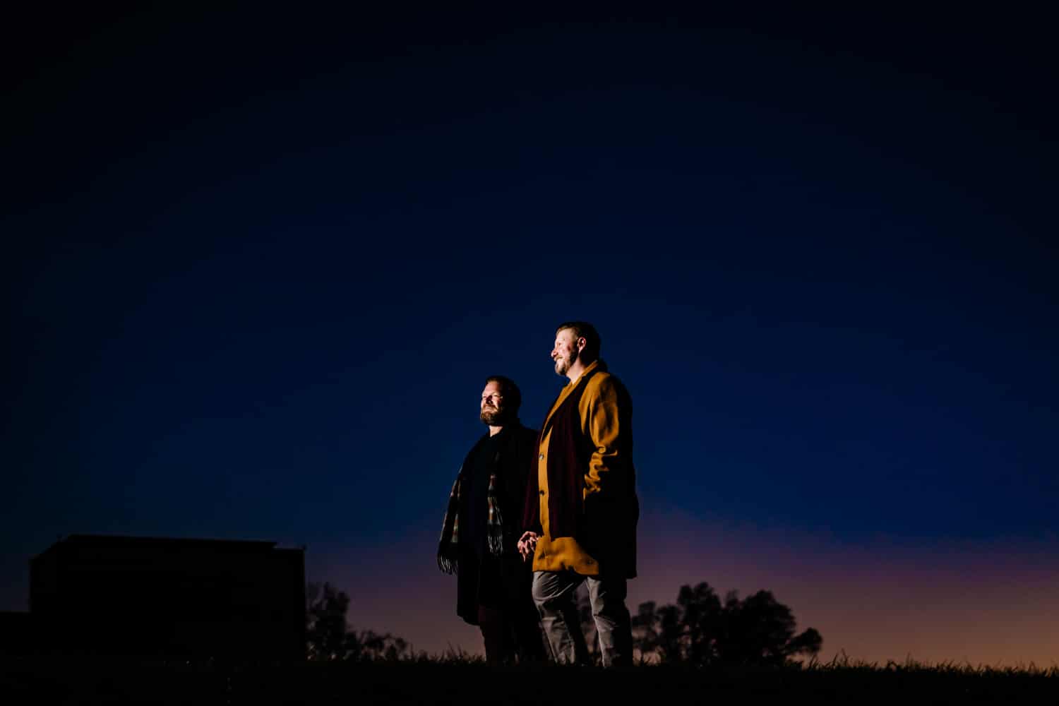 A candid portrait of an engaged couple holding hands and walking across a sunset sky during an evening engagement session at Liberty Memorial in Kansas City. 