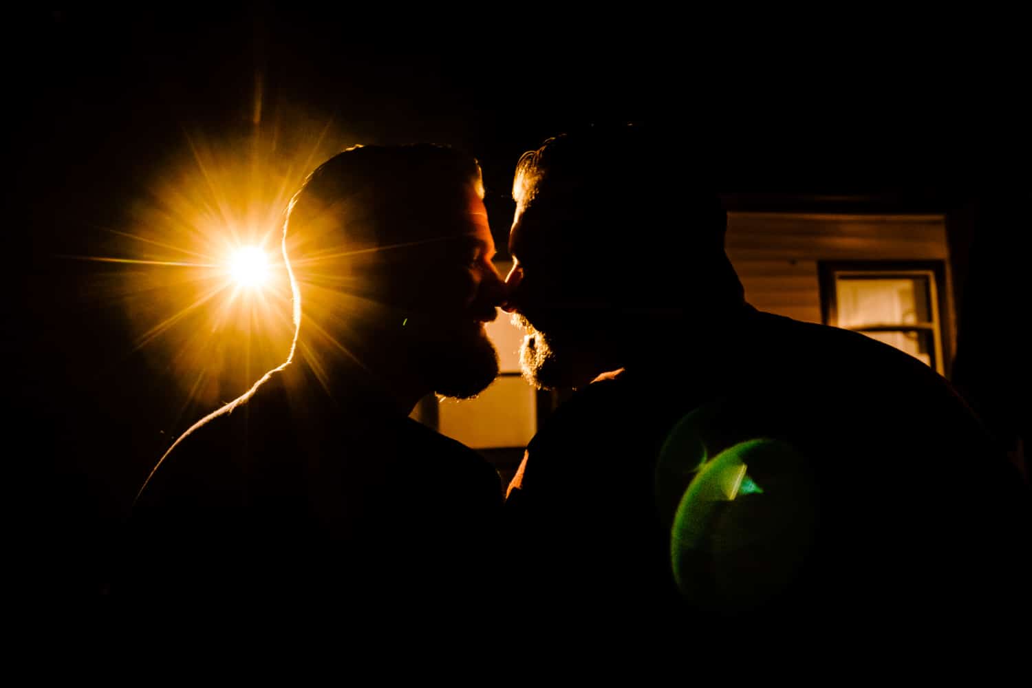 The silhouette of an engaged couple leaning in to share a kiss during an engagement session at home. 