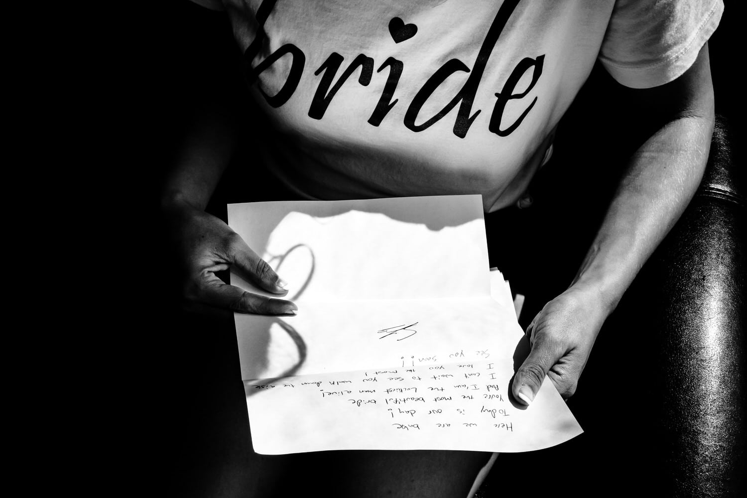 A bold black and white picture of a woman in a "bride" teeshirt holding and reading a letter from her groom on the day of her intimate church wedding ceremony in Kansas City. 