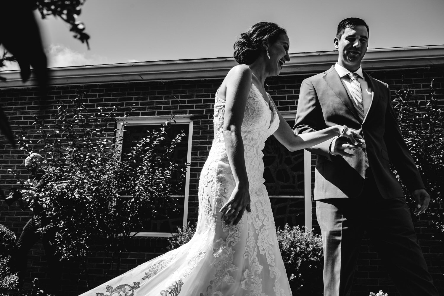 A candid, black and white picture of a bride and groom holding hands, laughing together on the day of their intimate church wedding ceremony in Kansas City. 
