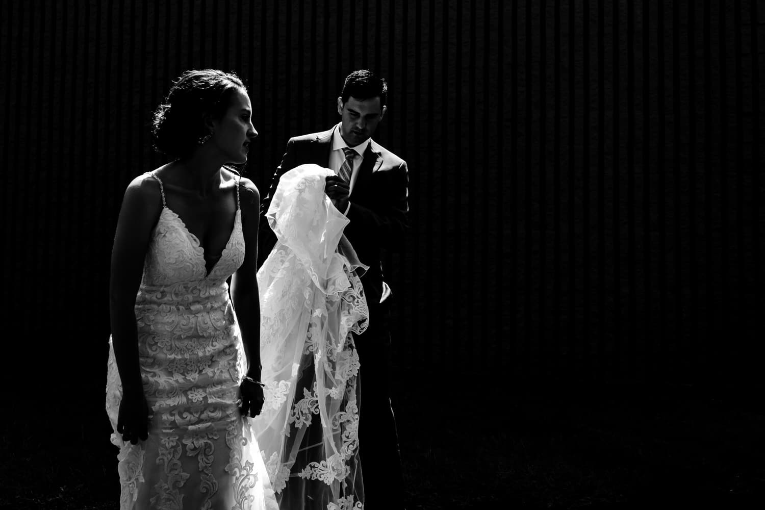 A dramatic black and white picture of a bride and groom leaning in to share a kiss against a solid black backdrop on their wedding day in Kansas City. 