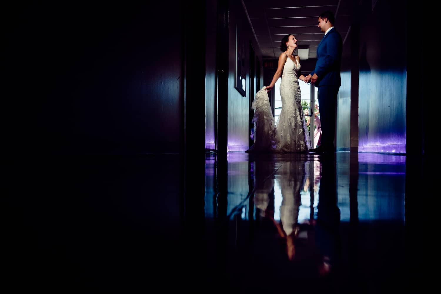 A colorful, candid portrait of a bride and groom dancing in a hallway painted with blue and purple color on the afternoon of their summer wedding day in Kansas City. 