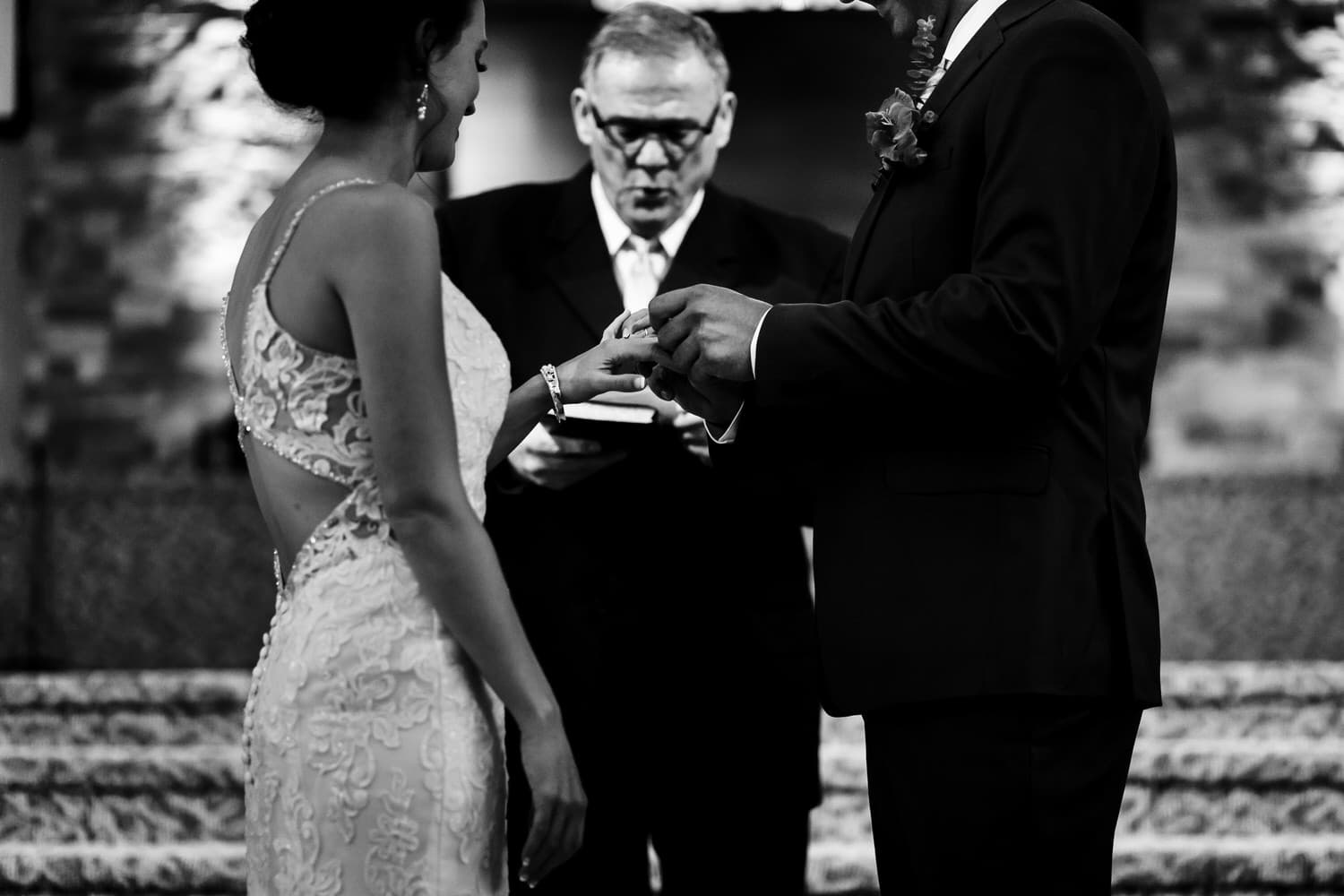 A candid black and white picture of a groom putting a wedding band on his bride's hand during their intimate church wedding ceremony in Kansas City. 