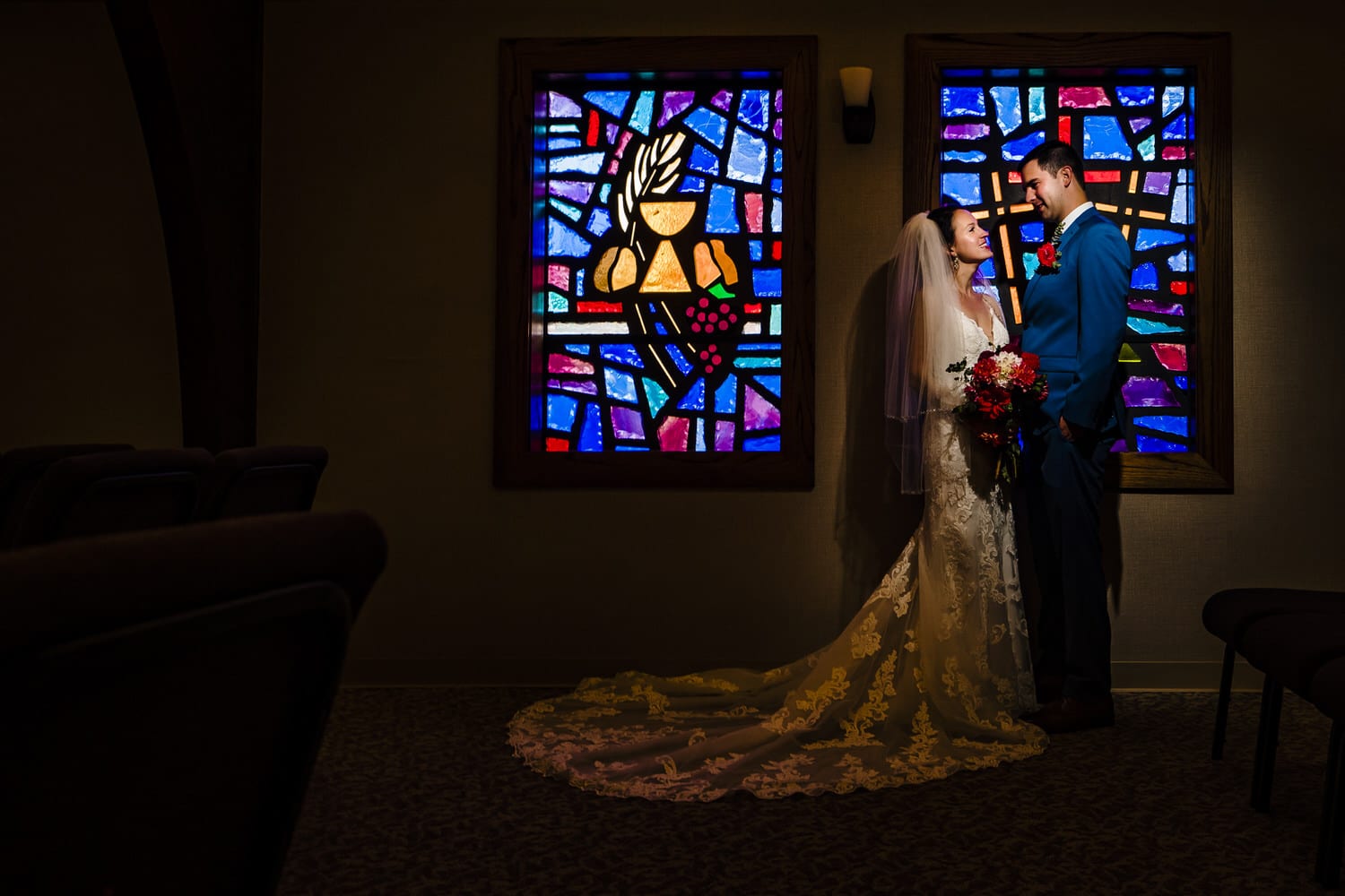 A colorful portrait of a bride and groom standing in front of a colorful stained glass window on the day of their intimate wedding ceremony in Kansas City. 