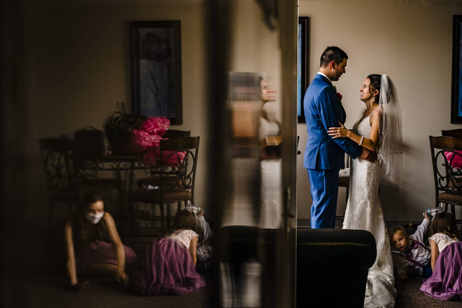 A colorful, candid picture of a bride and groom sharing a hug at the end of their wedding day as a flower girl and ring bearer crawl around on the floor beside them. 