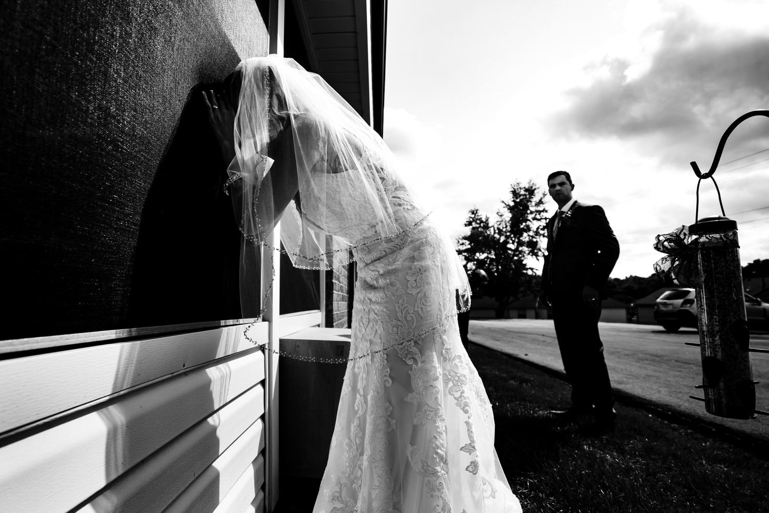 A candid black and white picture of a bride peeking into a window of a building. 