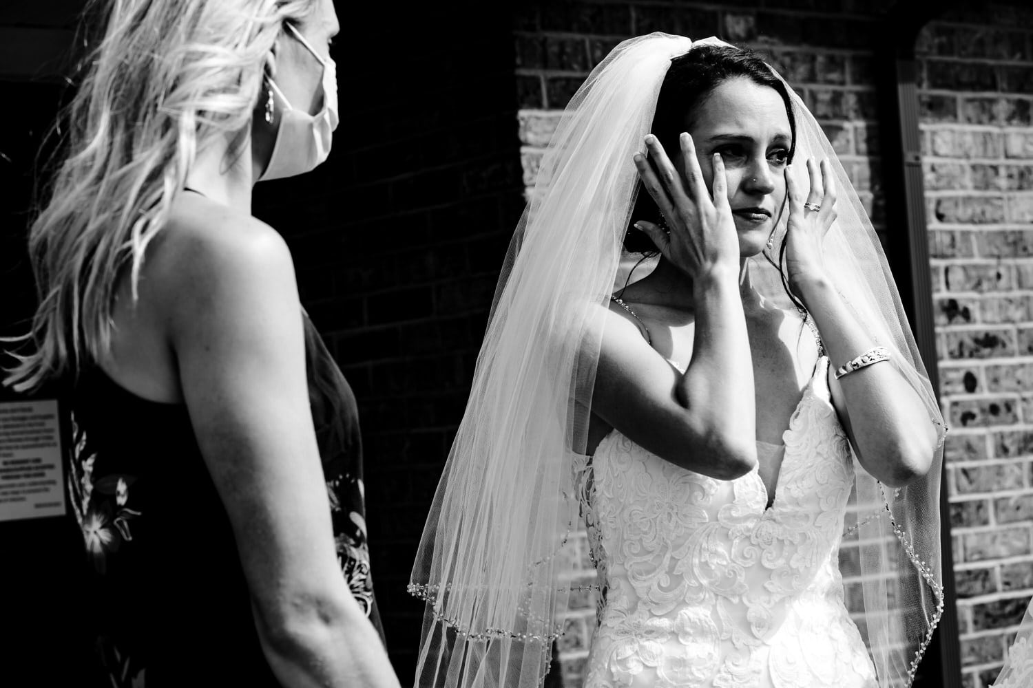 A candid black and white picture of a bride wiping tears from her eyes after seeing her dad on her wedding day. 