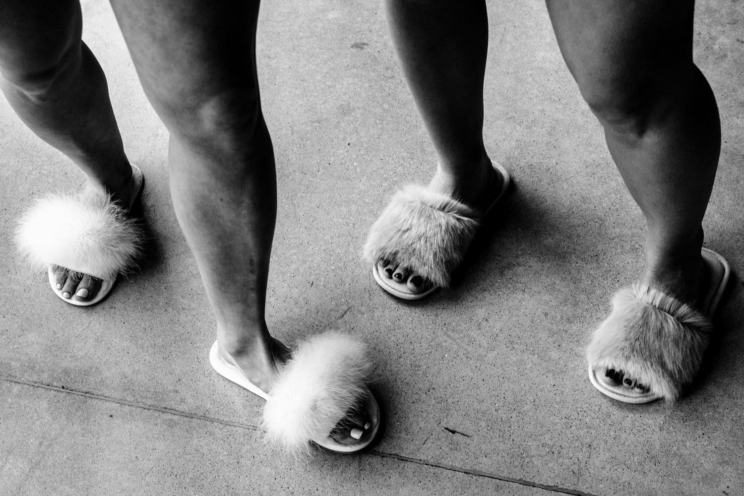 A black and white picture of two sets of women's legs in fuzzy slippers on the morning of a timeless spring wedding at The Farmhouse kC Event Venue.