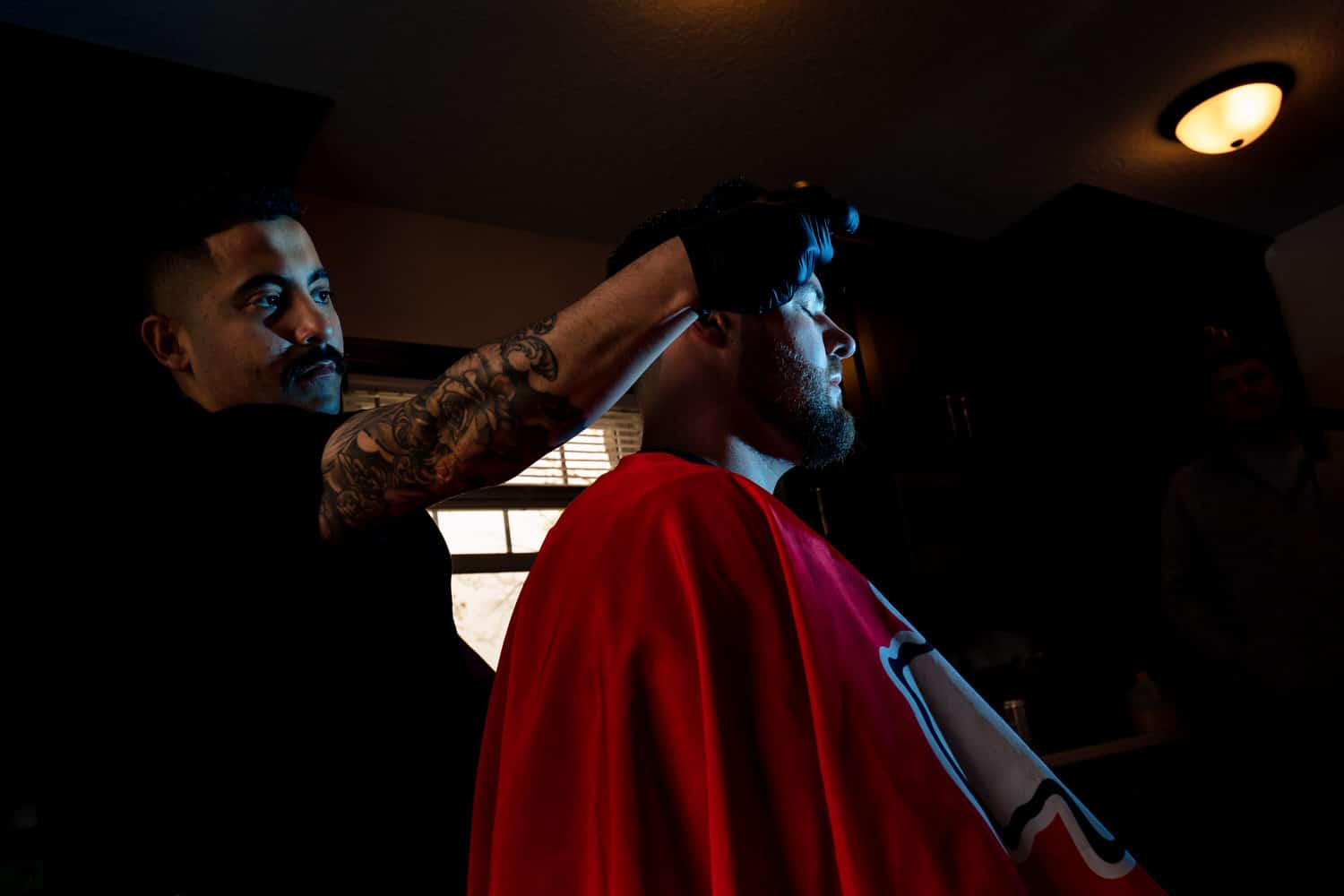 A dramatic, candid picture of a barber giving a man a haircut in The Cottage at The Farmhouse KC Event Venue. 