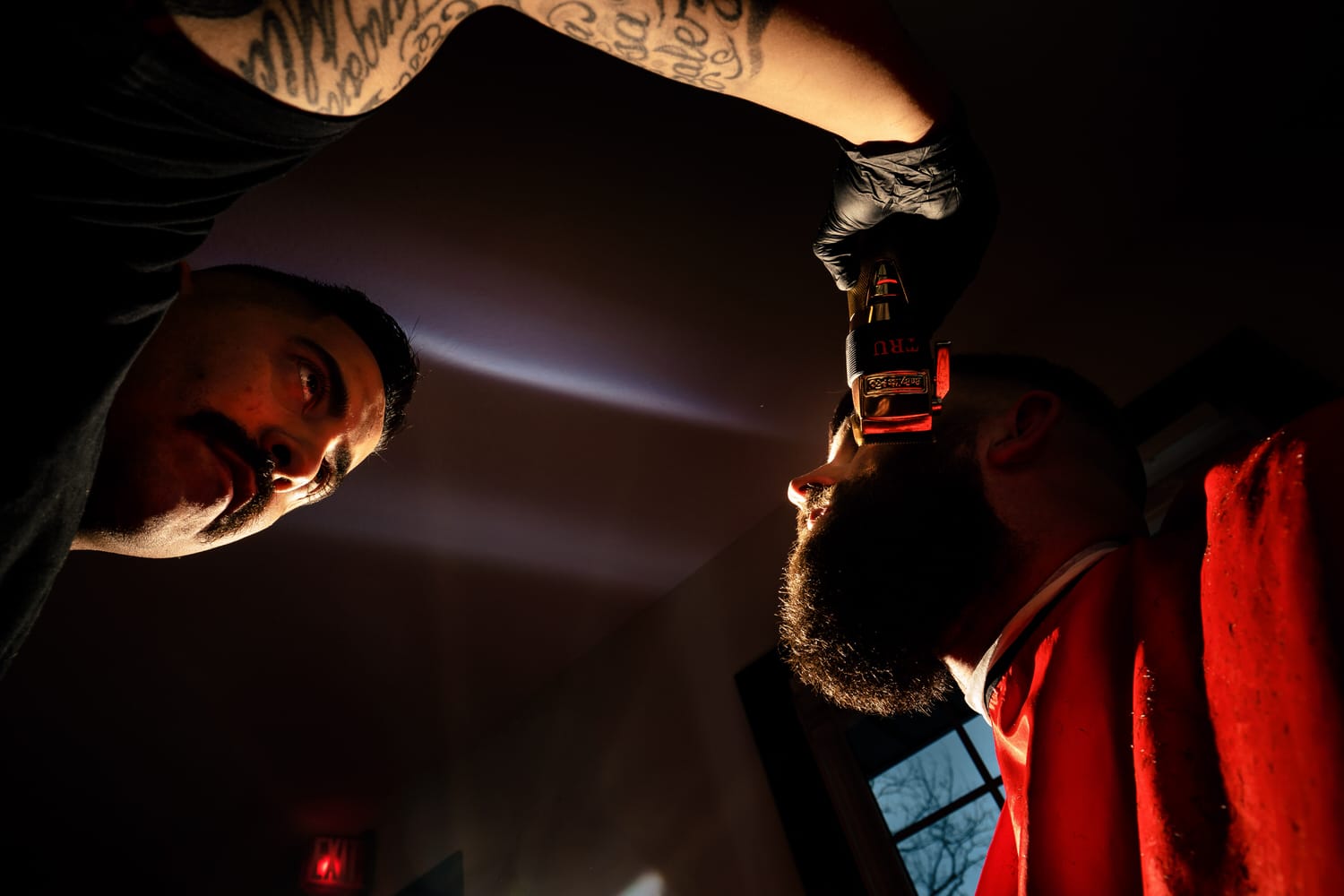 A colorful, candid picture taken from the ground looking up of a barber shaving a man's sideburns on the morning of his wedding at The Farmhouse KC Event Venue. 