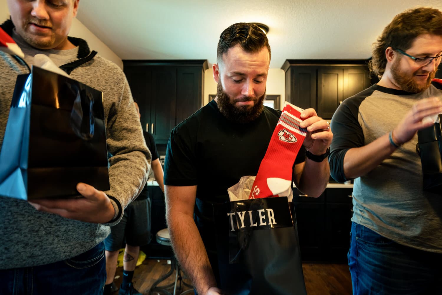 A colorful, candid picture of a man opening a gift that contains a pair of red Chiefs socks on the morning of a spring wedding in Kansas City. 