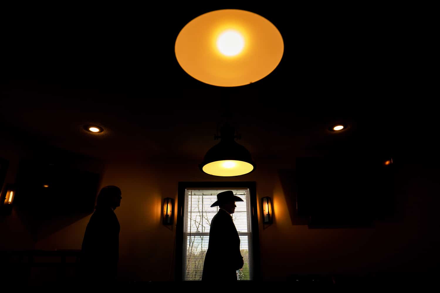 A colorful silhouette of a man in a cowboy hat standing underneath a light. 