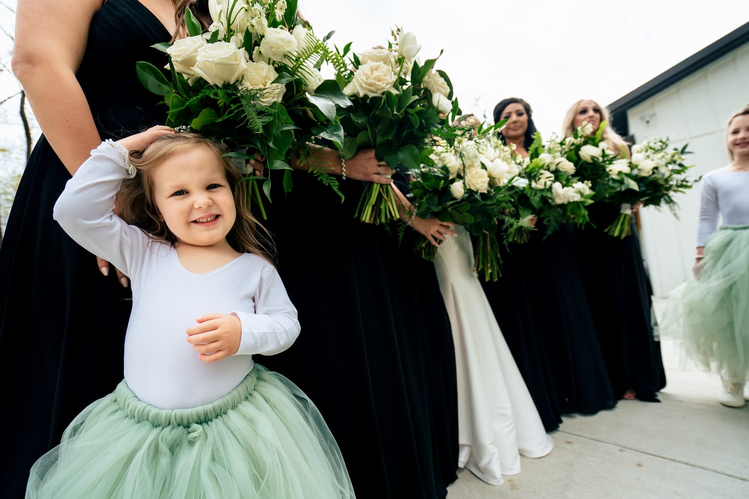 A candid picture of a tiny flower girl leaning against a group of bridesmaids, hiding underneath their bouquets on a spring wedding day. 