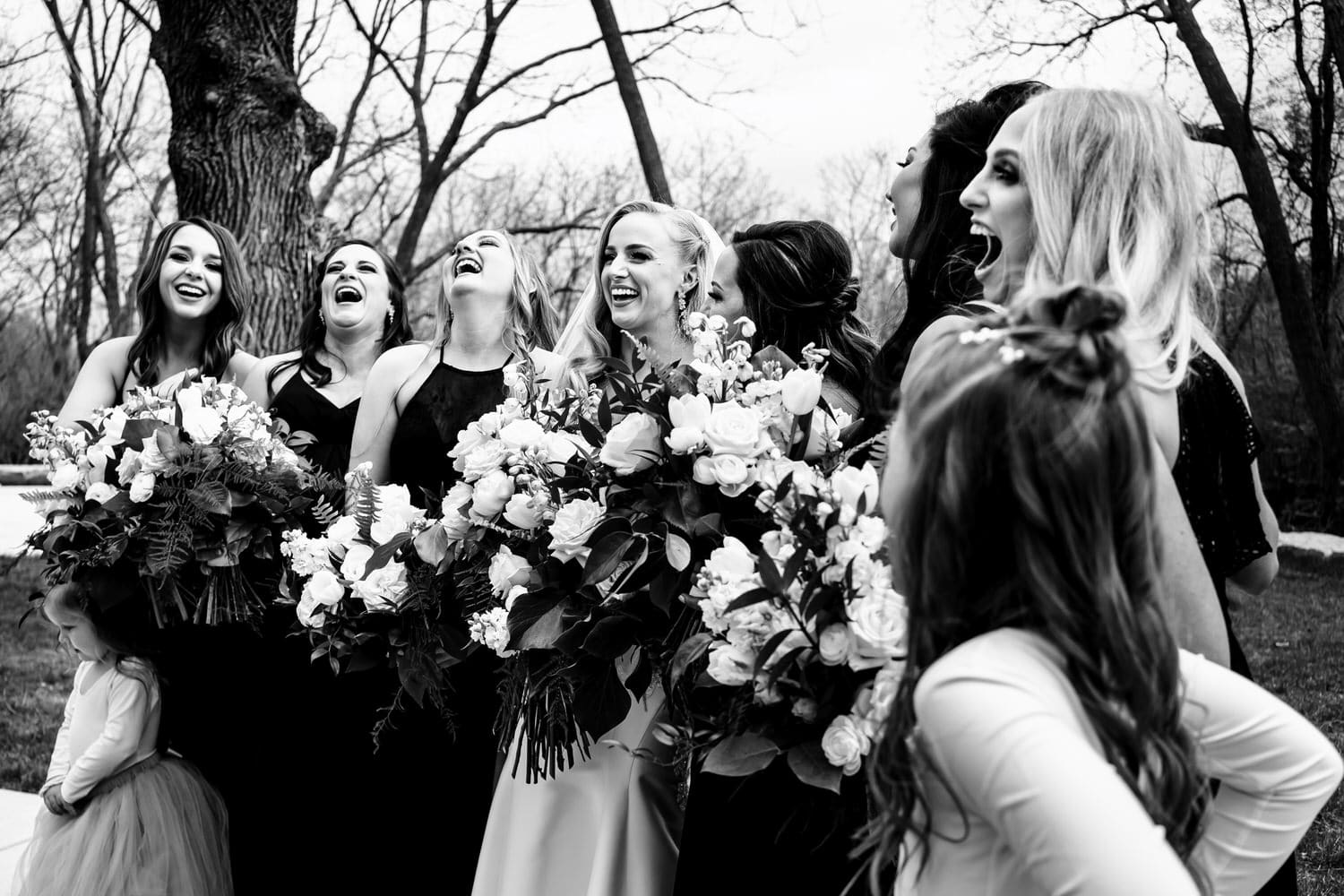 A candid black and white picture of a group of bridesmaids with their heads thrown back laughing on a spring wedding day at The Farmhouse Event KC. 