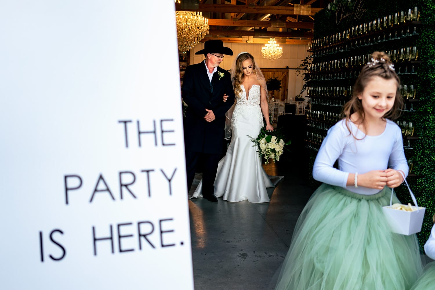 A candid picture of a flower girls tarting her walk down the aisle, while a bride and her dad wait in the background moments before a spring wedding at The Farmhouse KC Event Venue. 