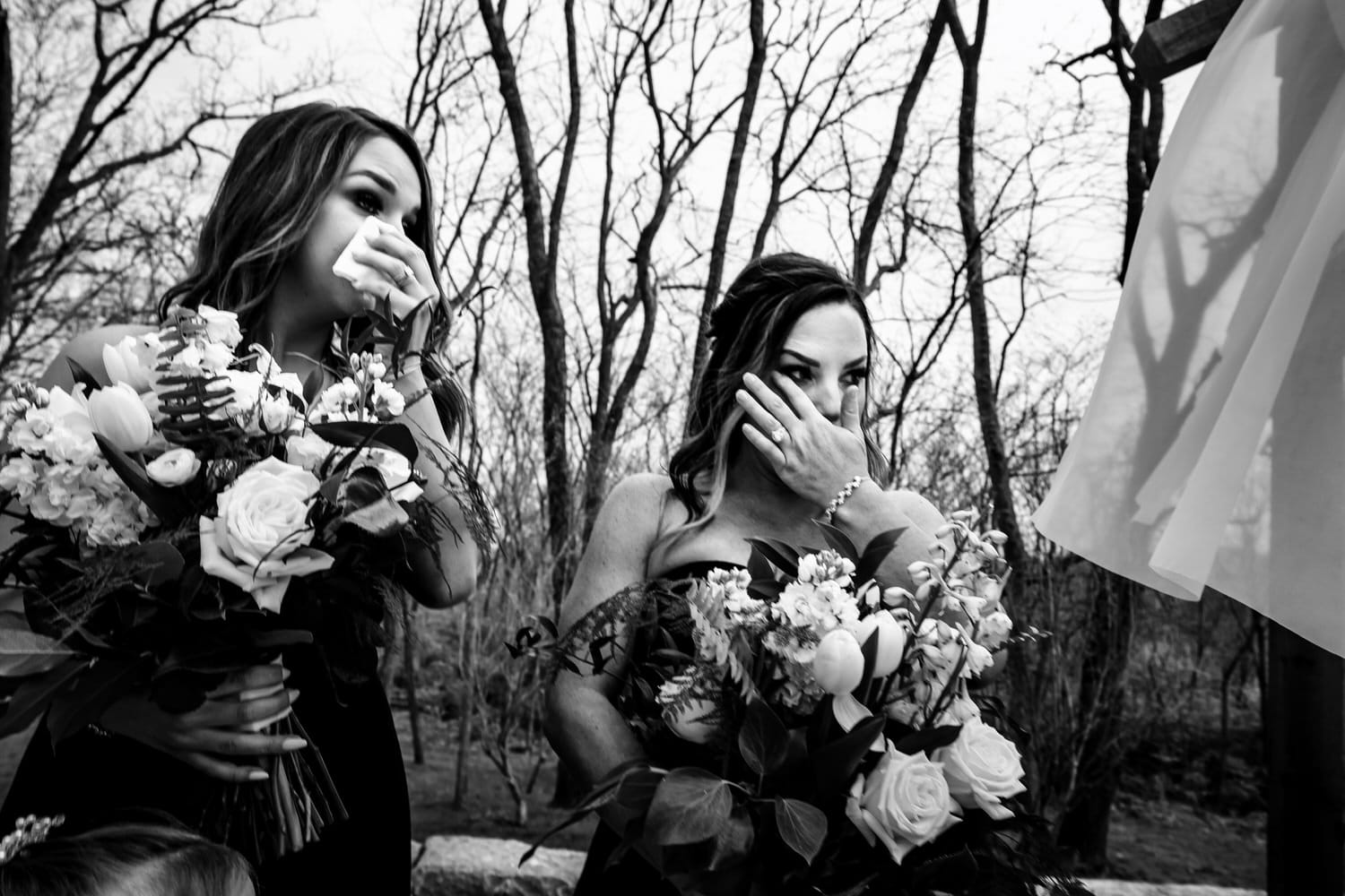 A candid black and white picture of two bridesmaids wiping tears from their eyes during a spring wedding ceremony in Kansas City. 