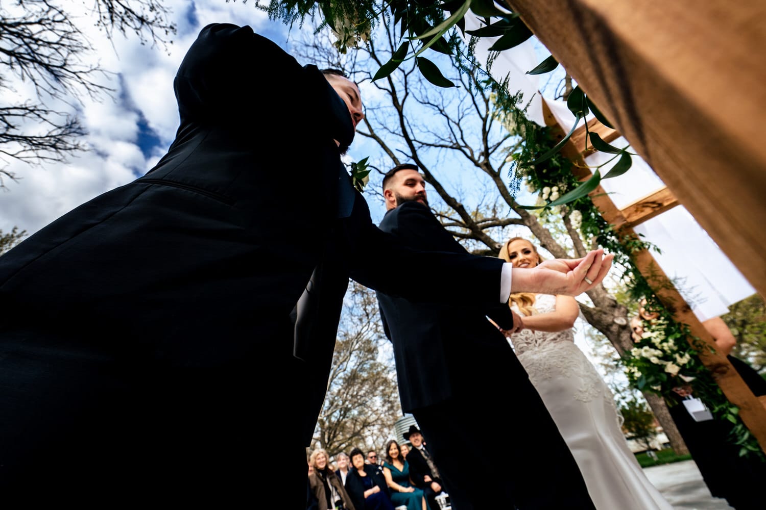 A candid picture taken very close-up of a best man reaching out to a wedding officiant with wedding bands in his hands. 