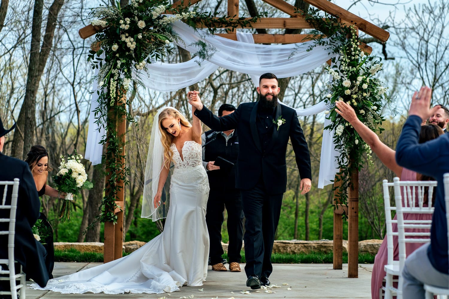 A candid picture of a bride and groom, their arms up in celebration walking up their aisle after their wedding ceremony at The Farmhouse KC Event Venue. 