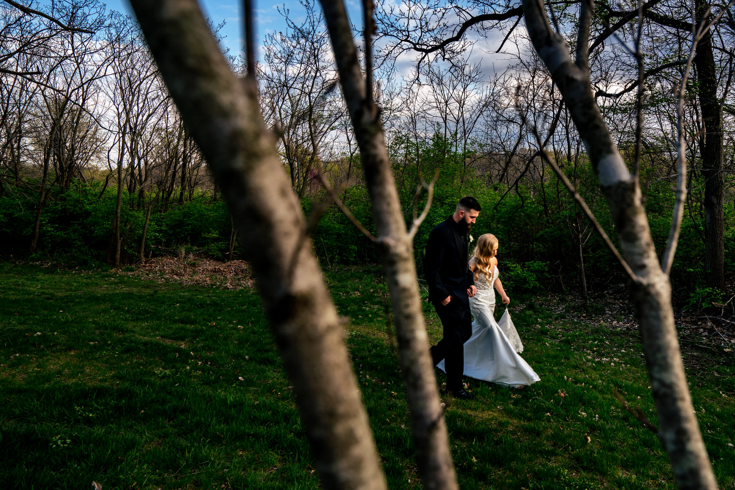 A colorful, candid picture of a bride and groom walking hand-in-hand across the back yard of The Farmhouse KC.