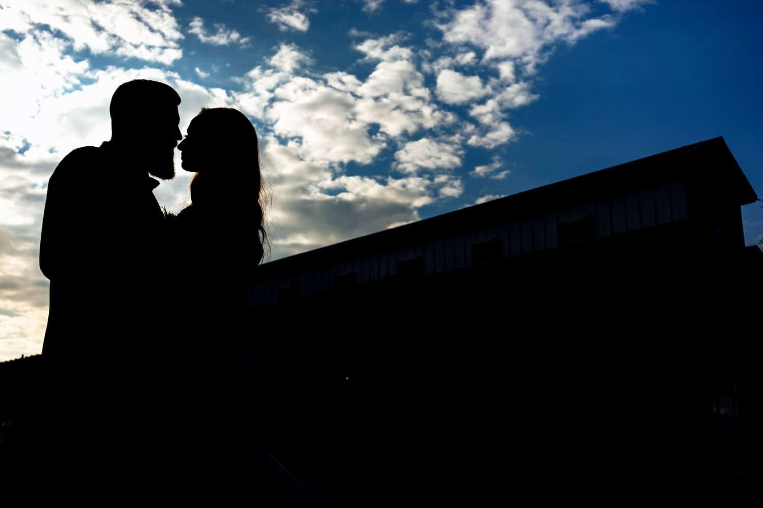 A colorful silhouette of a bride and groom standing against the outline of The Farmhouse KC Event Venue. 