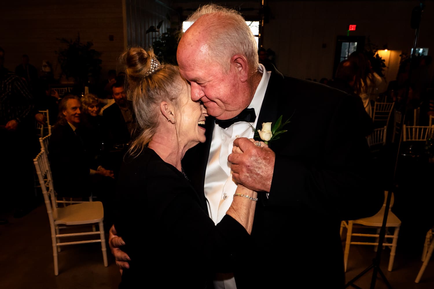 A close-up, candid picture of a groom's grandparents dancing and laughing together during the anniversary dance at a wedding reception. 
