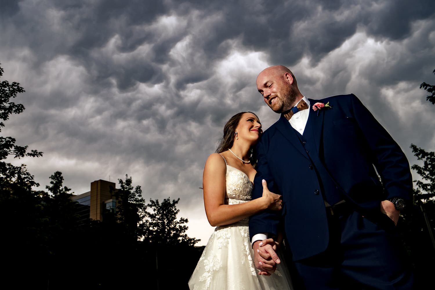 A dramatic portrait of a bride squeezing on to her groom's arm as he smiles down at her on the afternoon of their summer wedding at The Bride and the Bauer in Kansas City's Crossroads District. 