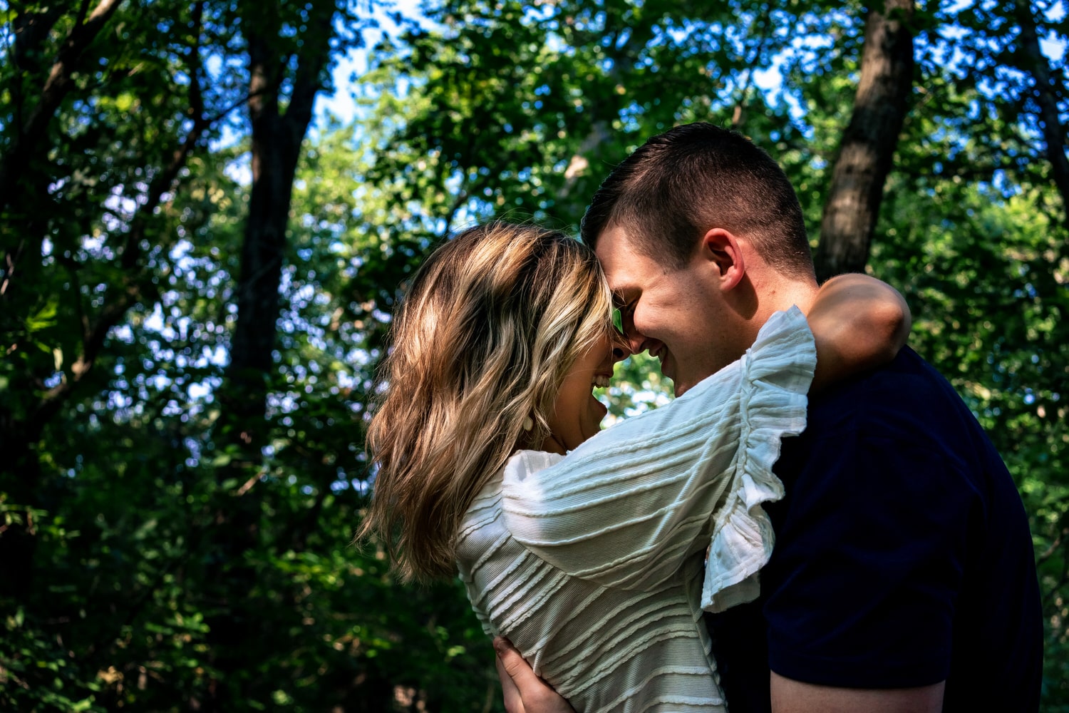 A colorful portrait of an engaged couple sharing a kiss in the middle of a green forest during their engagement session at Powell Gardens. 