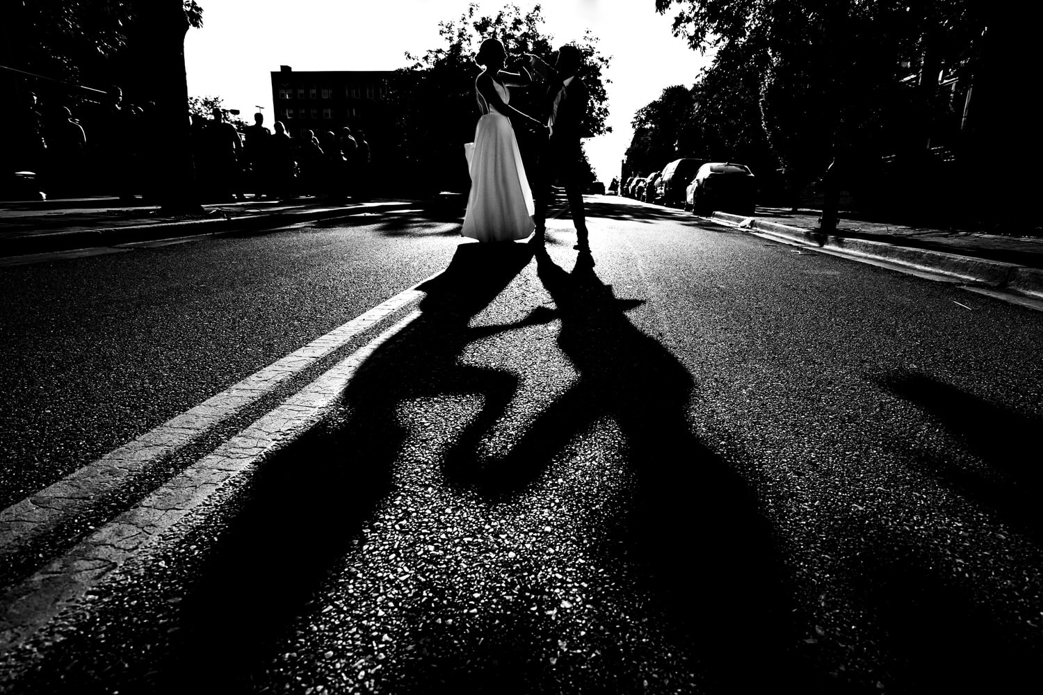 A candid black and white picture of a bride and groom dancing in the middle of the street, their shadows visible on the street in front of them on a summer wedding day in Kansas City. 