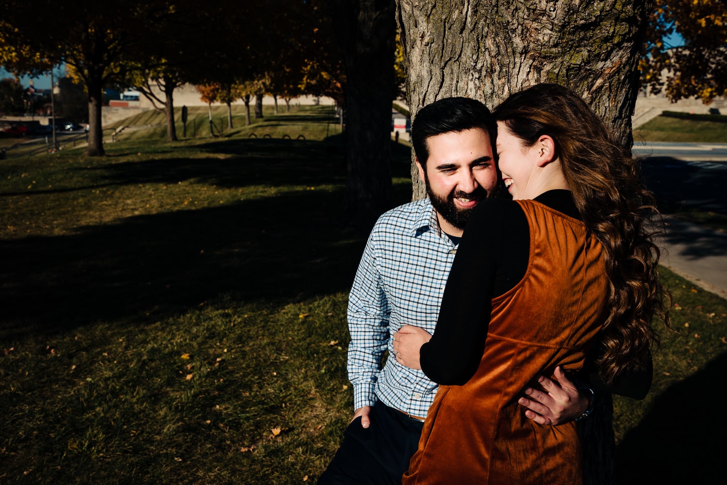 A candid, colorful picture of an engaged couple sharing an embrace underneath a colorful tree during an engagement session at Liberty Memorial in Kansas City. 