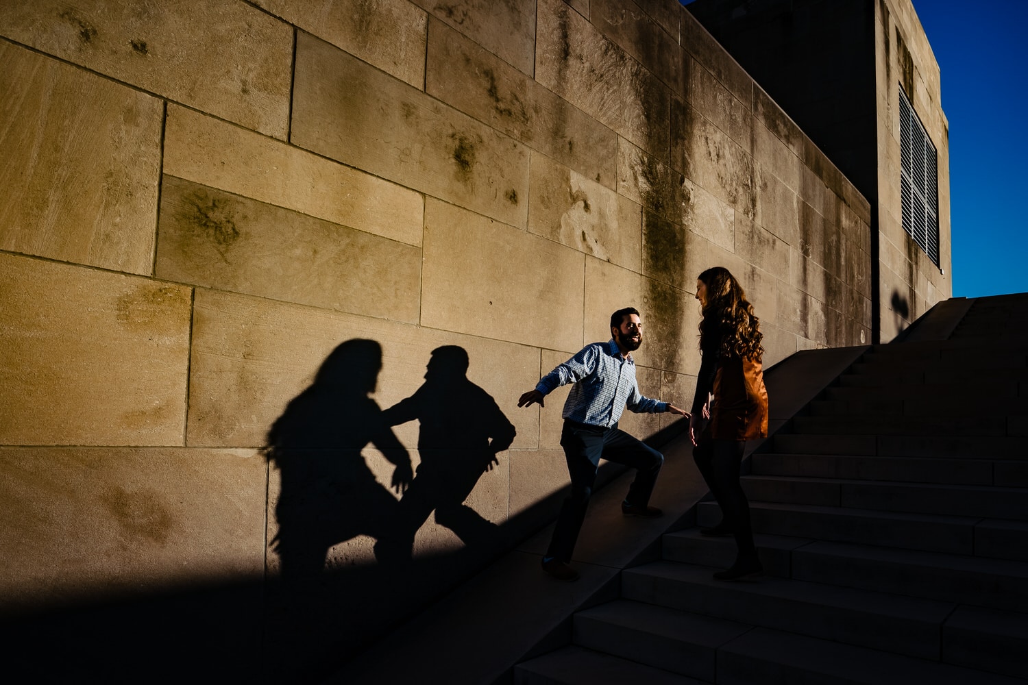 A candid picture of a man and woman dancing, their shadows visible on the wall beside them during a fall engagement session at Liberty Memorial. 