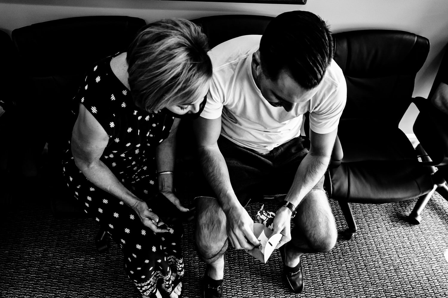 A candid black and white picture of a groom sitting with his mom opening a gift on the morning of his wedding in Kansas City. 