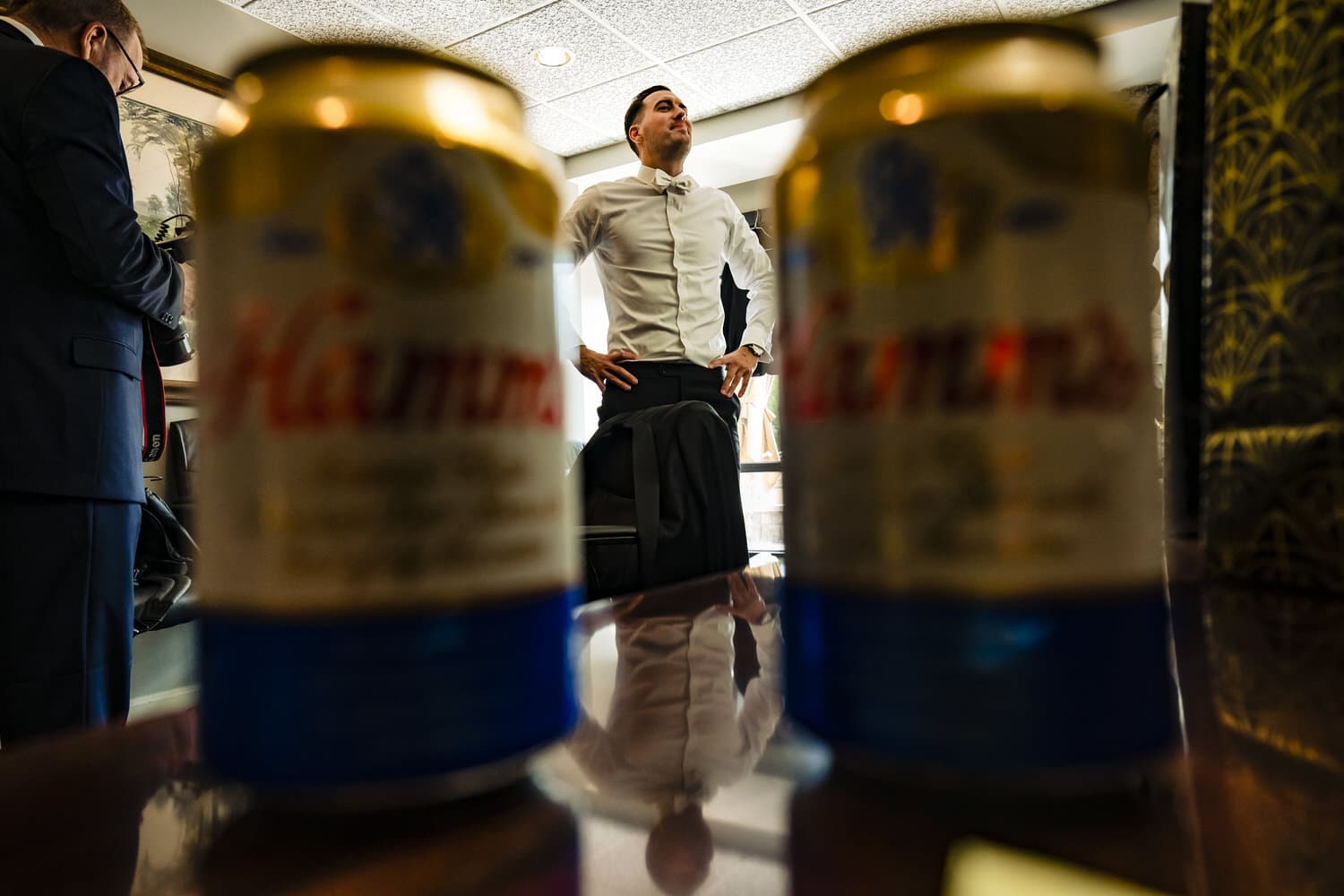 A colorful picture of a groom standing with his hands on his hips, two cans of Hamms visible on the table in front of him. 