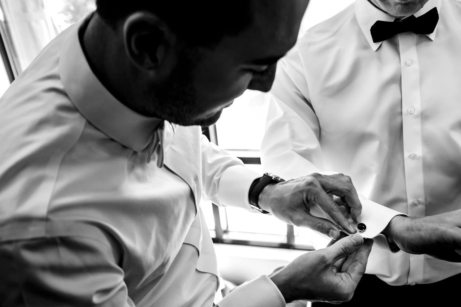 A candid picture of two men working to put on a pair of cuff links on a fall wedding day. 