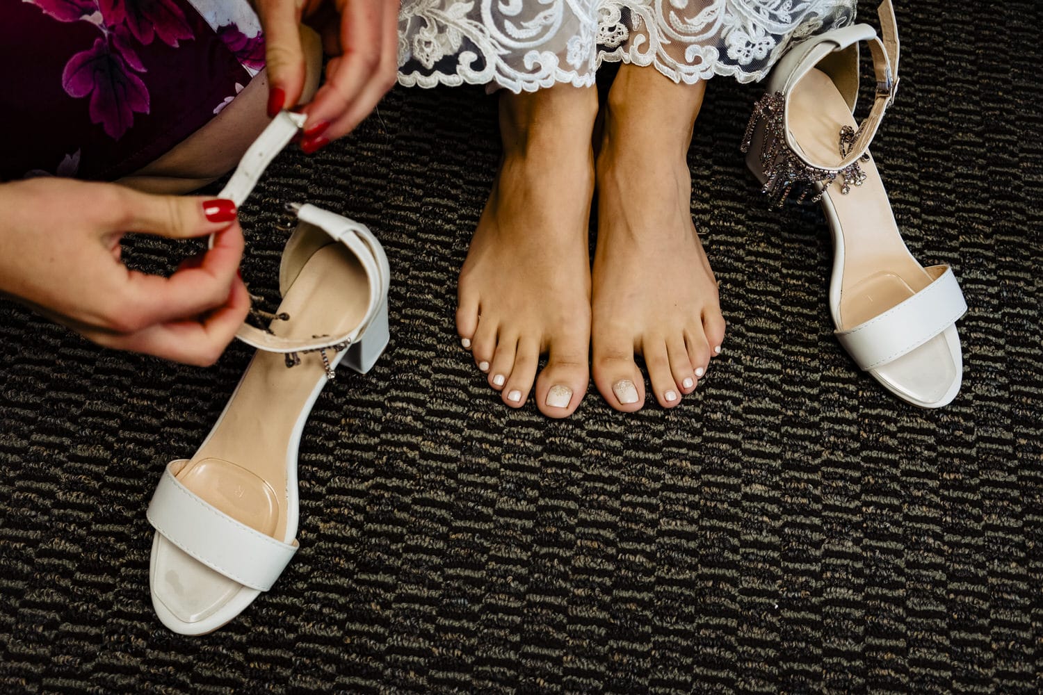 A candid, colorful picture of a woman's feet, a pair of hands getting ready to put shoes on the feet. 