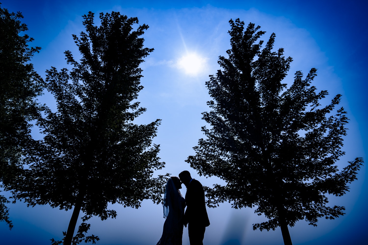 A candid, colorful silhouetted picture of a bride and groom leaning in for a hug seconds after their first look on their fall wedding day in Kansas City. 