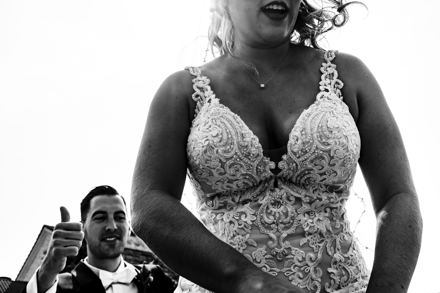 A candid picture of a bride climbing into a car, her mouth opening in a smile, her groom giving a thumbs up behind her. 